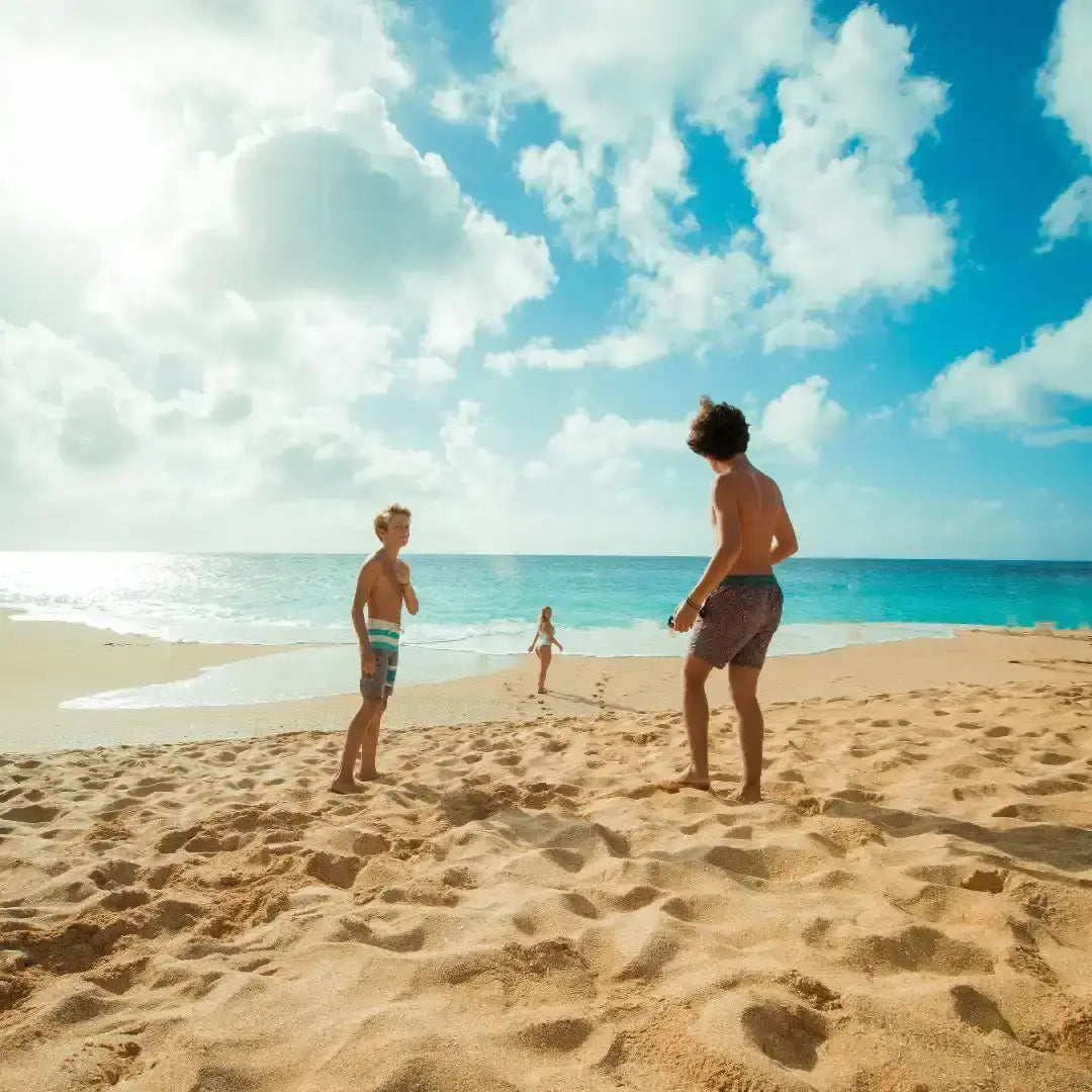 Two adults and a child playing on a sandy beach with clear blue sky and ocean.