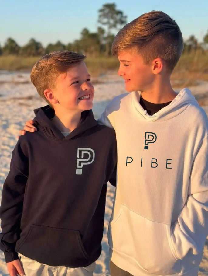 Two children wearing hoodies with a PIBE logo on a beach