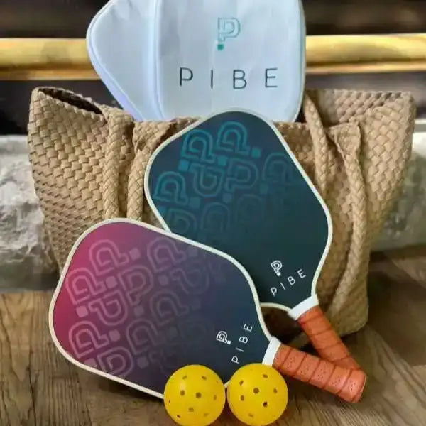Two pickleball paddles with orange handles and a white paddle cover labeled 'PIBE' on a wooden surface.