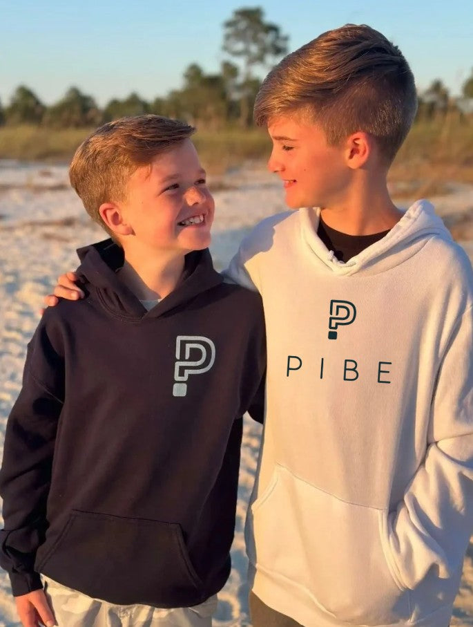 Two children wearing hoodies with a PIBE logo on a beach