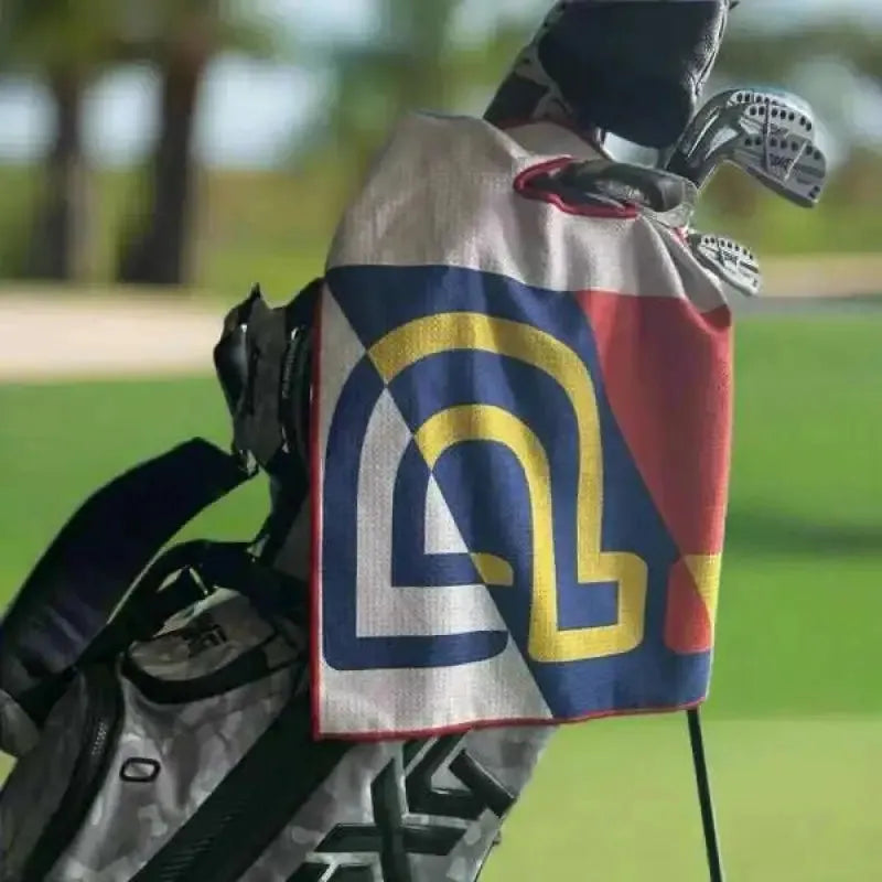 Golf bag with a colorful towel featuring PIBE on a blurred golf course background